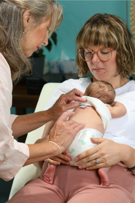 A woman holding a baby while another woman holds it.